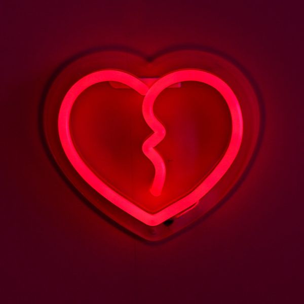 Custom Neon® Red Broken Heart Light Up Wall Art shown illuminated against a dark pink wall in dim light