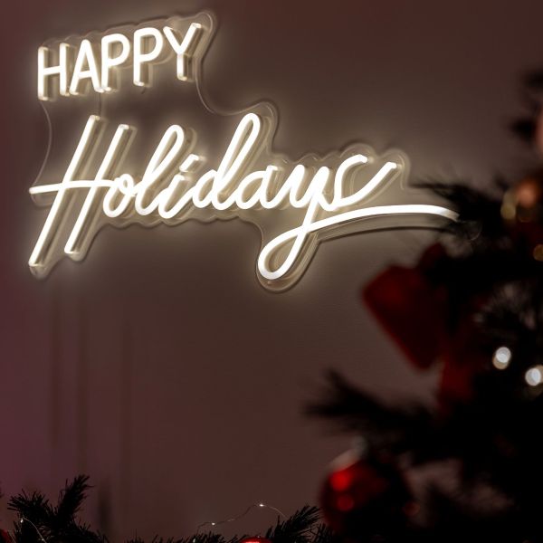 CUSTOM NEON® Happy Holidays warm white LED neon sign wall-mounted next to a Christmas tree