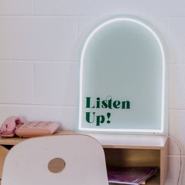 Listen Up! white & green neon art shown as a desk light in a dorm room @customneon Signs of Change charity range