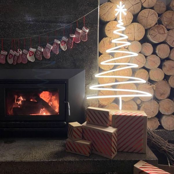 Warm white light up neon Xmas tree surrounded by a modern wood fireplace, Christmas stockings & presents - by CUSTOM NEON® 