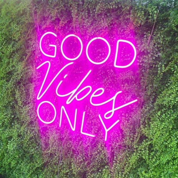 Good Vibes Only Trendy LED Neon Light in Two Fonts shown in pink on green wall from Custom Neon®
