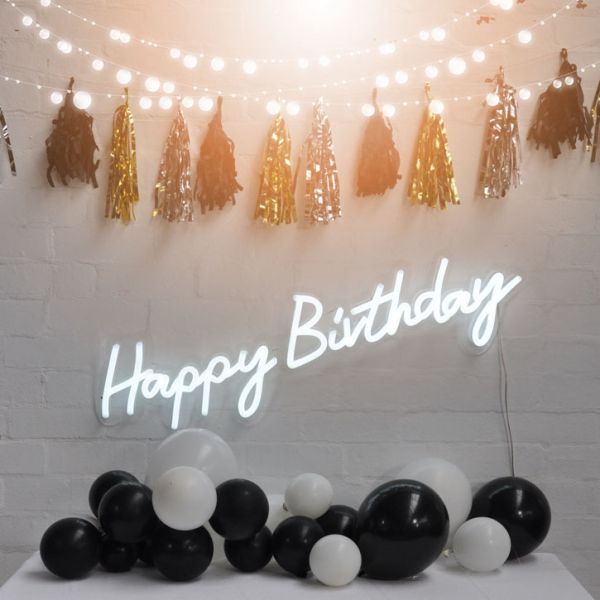 Happy Birthday illuminated sign from Custom Neon, shown on brick wall with party decorations.