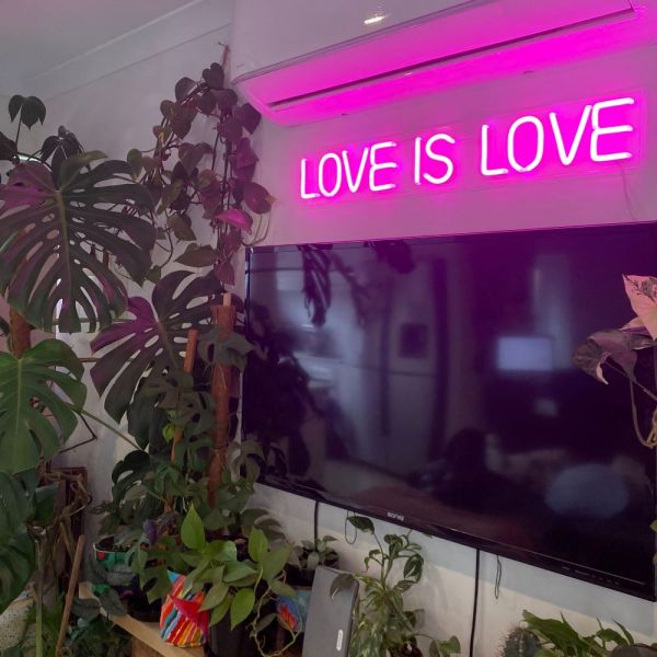 Custom Neon® pink LOVE IS LOVE light sign shown wall mounted above a TV in a living room,Custom Neon® signs and artwork mounted above a bed,LED neon bedroom signs by Custom Neon®
