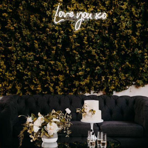 Love You XO LED neon sign on a green photo wall with a floral arrangement and cake in the foreground  - sign by CustomNeon.com / photo by candileonardphotography.com