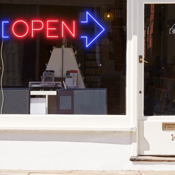 Neon light open sign in red with an oversized blue arrow shown in a shop window - from CustomNeon.com