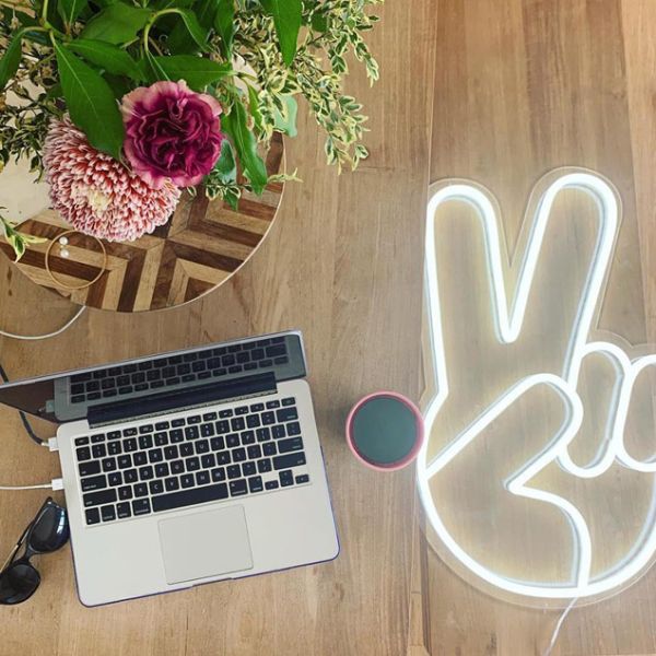LED Neon Peace Sign Light shown on wooden floor - Photo CustomNeon.com