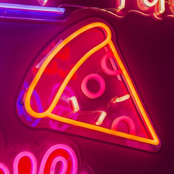 Custom Neon food sign: Pizza slice shown illuminated against a dark wall in dim light
