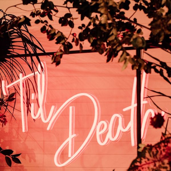 Til Death LED neon sign shown hanging from a frame at a wedding - photo from CustomNeon.com