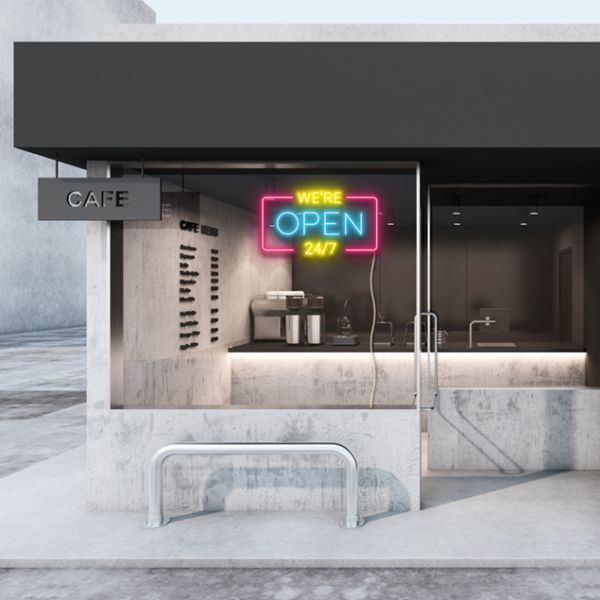 WE'RE OPEN 24/7 neon sign in yellow, blue & pink shown in a cafe window - from CustomNeon.com
