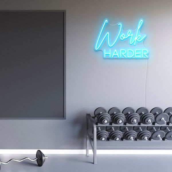 CUSTOM NEON® Work Harder sign in light blue on grey wall above weights