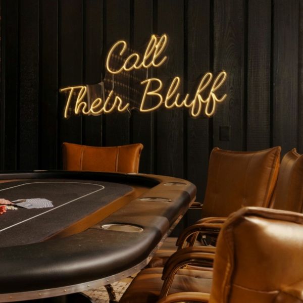 Call Their Bluff LED neon sign on a dark wooden wall behind a gaming table - CUSTOM NEON™ x SOMERLED COLLECTION