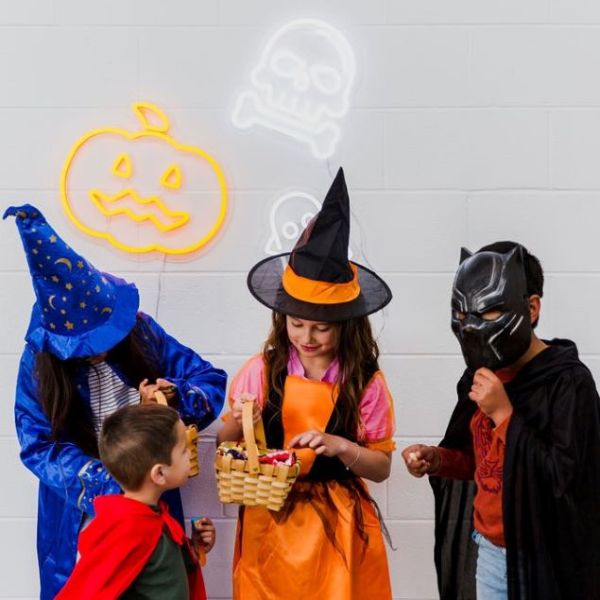 Cute LED neon ghost, skull & jack-o-lantern shown on a white brick wall with Halloween lights above kids in costumes - by Custom Neon®