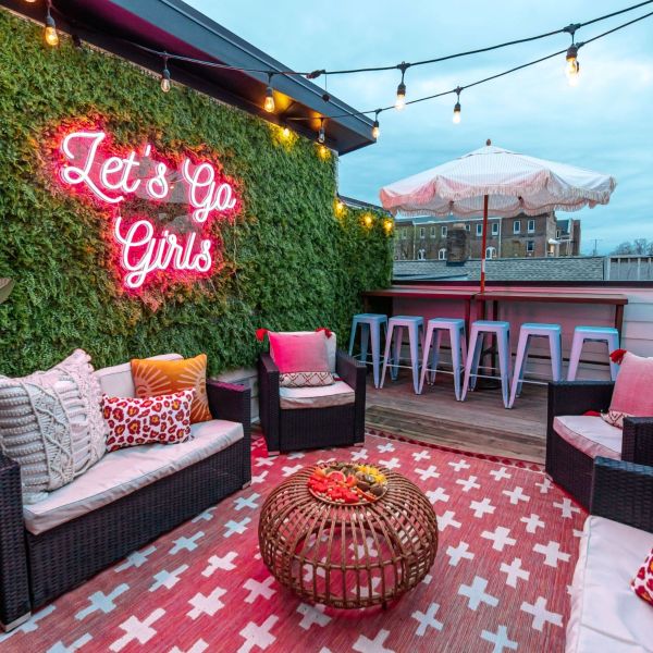 Let's Go Girls pink LED neon sign on a lush greenery wall on a balcony entertainment area - CUSTOM NEON™ x SOMERLED COLLECTION