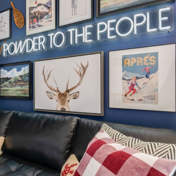 Powder to the People white LED neon sign on a blue feature wall surrounded by framed paintings and prints of mountain scenes - CUSTOM NEON™ x SOMERLED COLLECTION