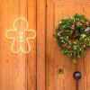 CUSTOM NEON® Gingerbread Man on wooden door beside a traditional Christmas wreath