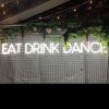 EAT DRINK DANCE large LED neon sign for events & weddings, shown on wire mesh with floral arrangement & fairy lights - photo from CustomNeon.com