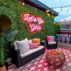 Let's Go Girls pink LED neon sign on a lush greenery wall in an alfresco seating area - CUSTOM NEON™ x SOMERLED COLLECTION