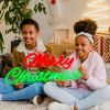 Merry Christmas Red & Green LED Neon Sign by CUSTOM NEON® held by smiling girls with a Nativity scene, presents & decorations in the background.