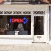 Neon light open sign in red with an oversized blue arrow shown in a shop window - from CustomNeon.com