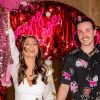 Crazy In Love Custom Neon® wedding sign in pink, styled against a red streamer background with the bride and groom in the foreground.