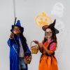 Cute LED neon ghost, skull & jack-o-lantern shown on a white brick wall with Halloween lights above kids in costumes - by Custom Neon®
