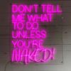 Don't Tell Me What to do Unless You're Naked pink LED sign from Custom Neon® shown on a white paneled wall