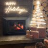 White LED neon Christmas tree & Happy Holidays sign mounted above a fireplace with wooden logs, presents & a basket of pinecones- by CUSTOM NEON® 