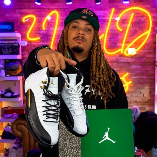 Sneaker collector holding Air Jordan 12s in front of a yellow script LED neon sign on a studio set