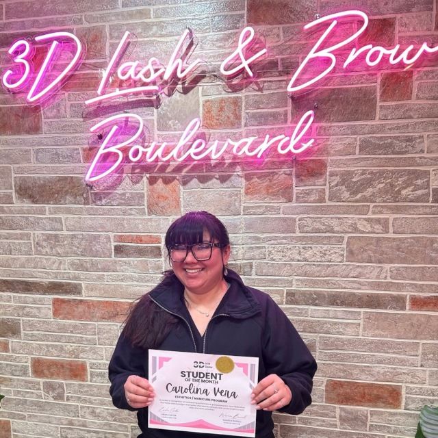 Student of the month holding her certificate under the pink 3D Lash and Brow Boulevard LED neon sign