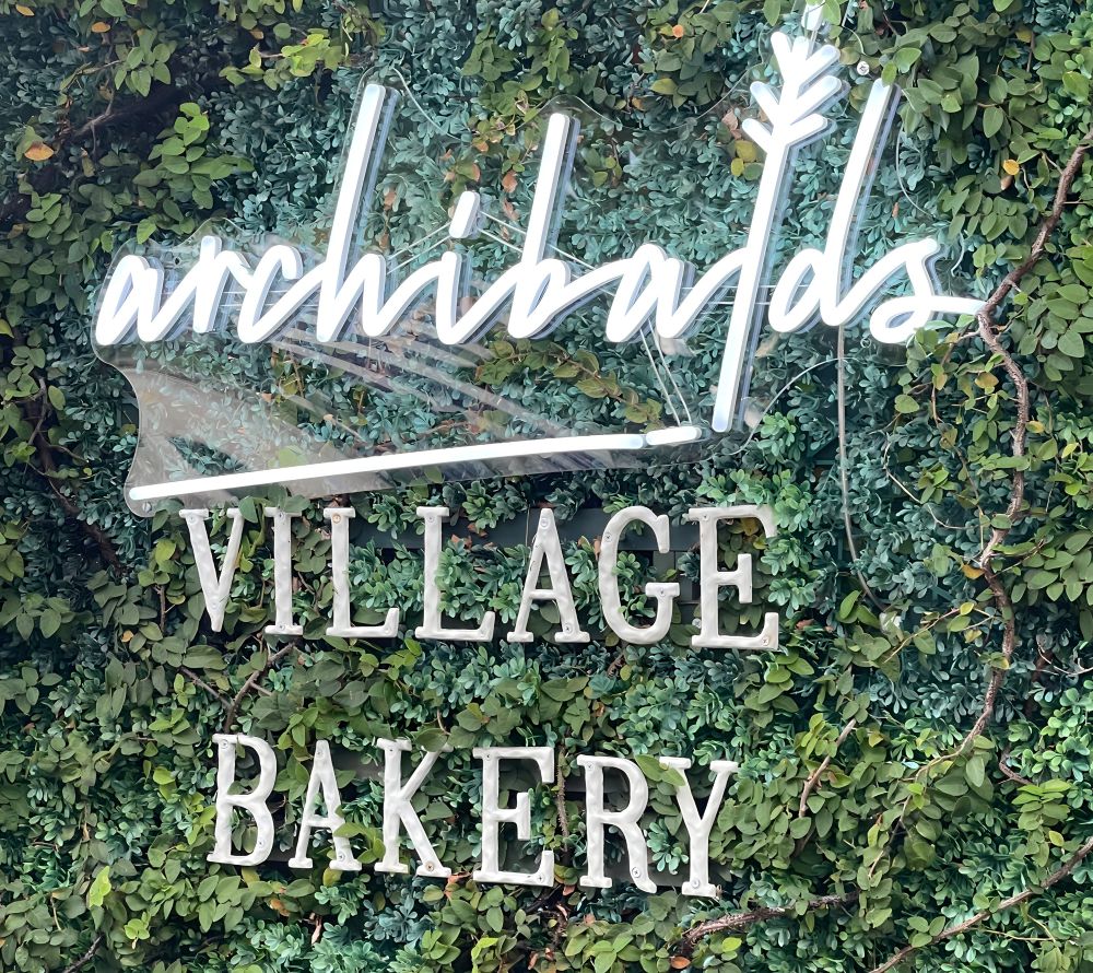 Archibalds Village Bakery Custom Neon® sign on a greenery wall at The North Beach Hotel in Fort Lauderdale FL