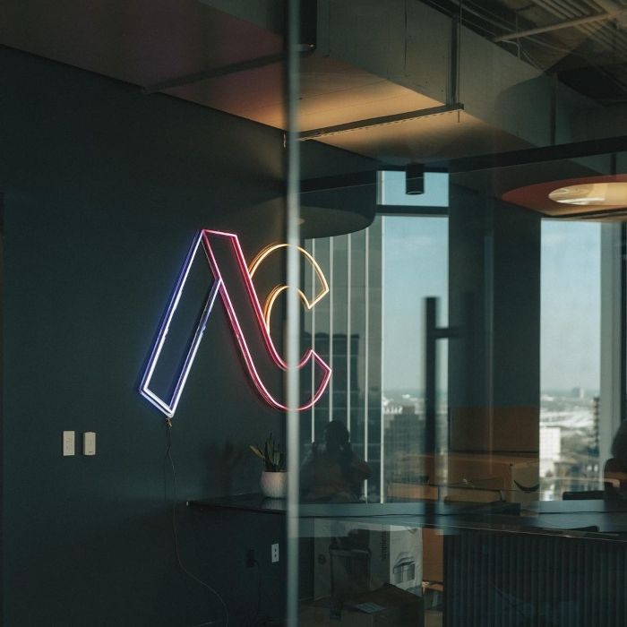 Multicolor AC logo LED neon sign in a high-rise Dallas office with skyline views through the window