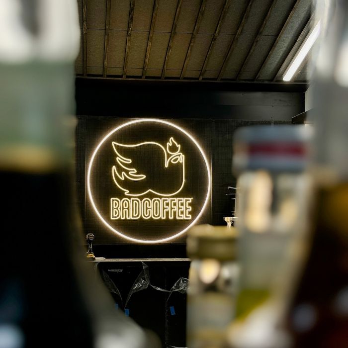 Custom Neon® sign for Bad Coffee glowing behind a row of bottles at the Chicago cafe