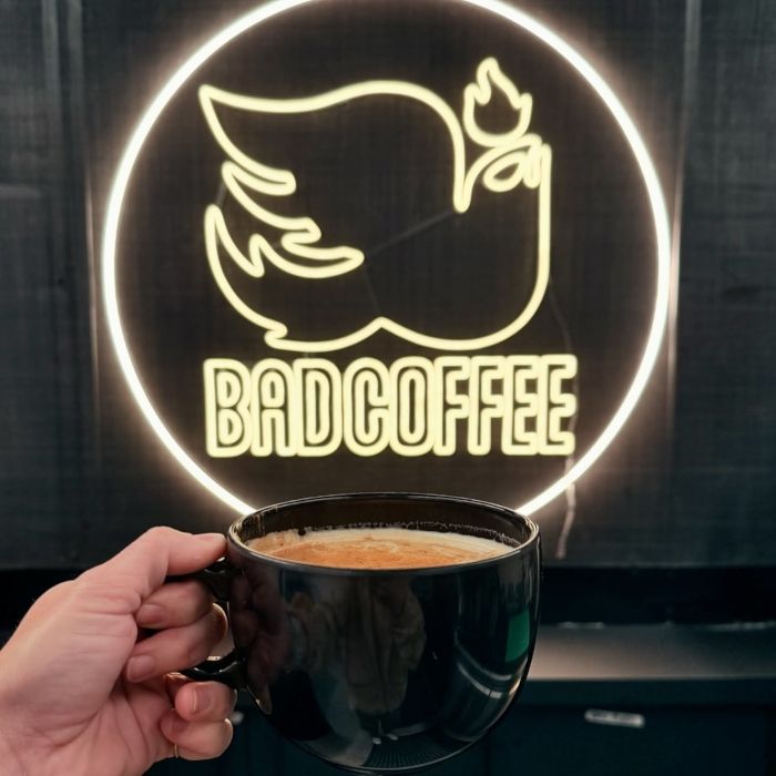 Bad Coffee Custom Neon® sign with a cup of coffee held up in front of it