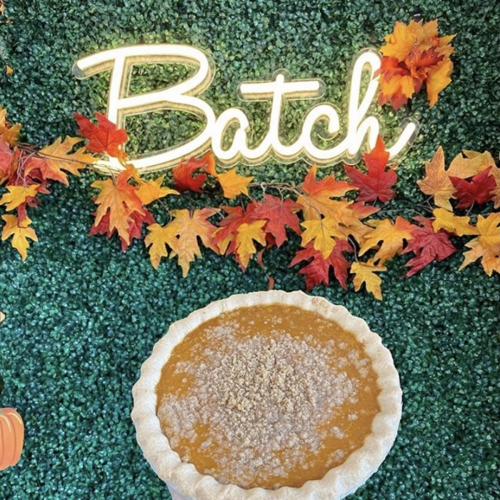 Warm white Batch script LED neon sign framed by autumn leaves above a pumpkin pie