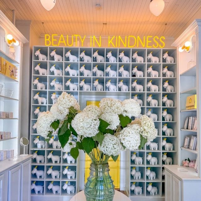 Beauty in Kindness yellow LED neon sign above shelves of white goat figurines in a skincare boutique