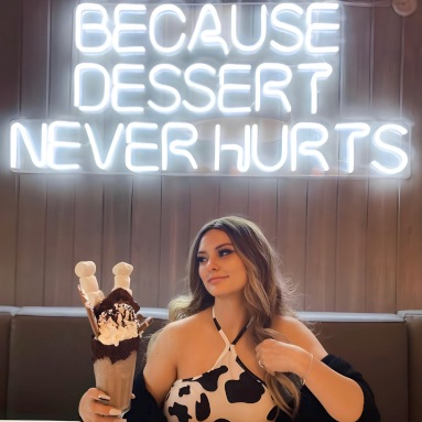 Because Dessert Never Hurts white Custom Neon® cafe sign on a wood paneled wall @mannysweetreats