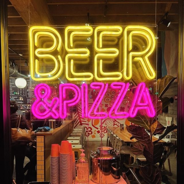 Yellow and pink custom neon 'Beer & Pizza' sign in a restaurant window