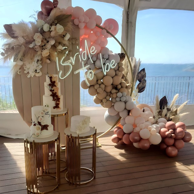 Custom Neon® white Bride to Be sign hung from a golden circular frame topped by pampas grass floral arrangement with a balloon waterfall and celebration cakes in the foreground - props and styling by @decorandfiesta
