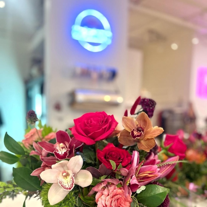 Custom Neon® UV Print logo on a white wall with a bouquet in the foreground @cedarhouseflowers