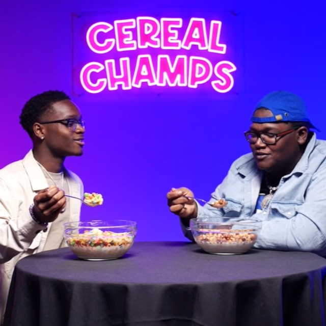 Cereal Champs pink LED neon sign glowing above two guests eating cereal on the show's set