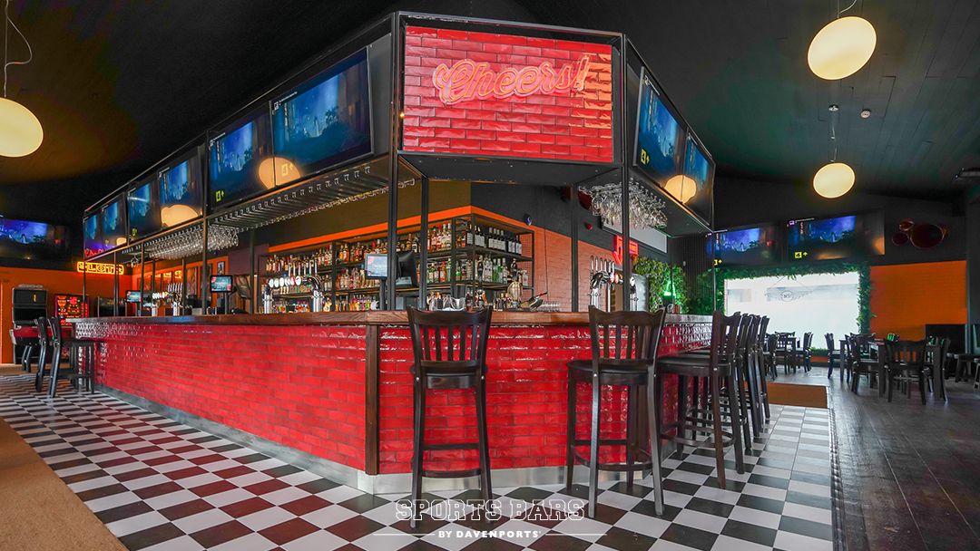 Wide angle view of a Davenports sports bar with red white and black check decor and a large red Custom Neon® sign above the bar that reads CHEERS