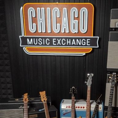 Chicago Music Exchange Custom Neon® sign on a dark wood paneled wall above amps and guitars