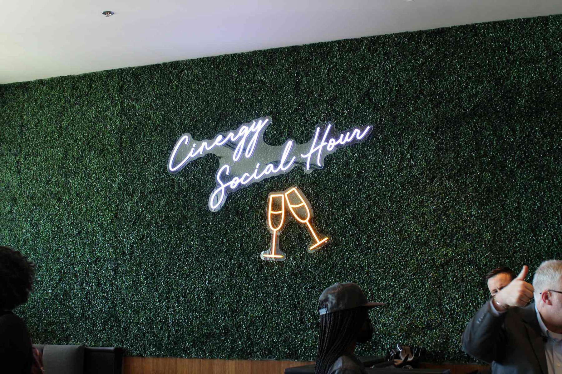 Cinergy Social Hour LED neon sign with orange champagne glasses on a greenery wall at a cinema lounge