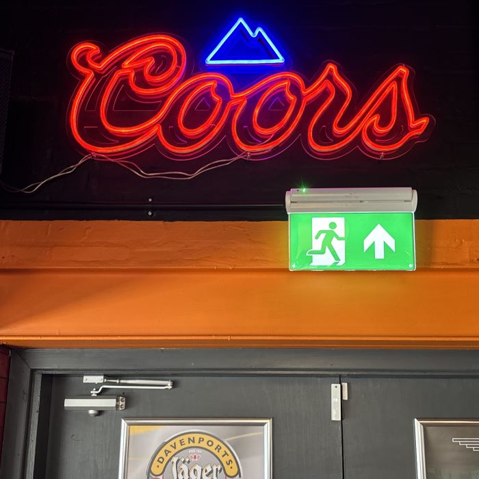 Custom red LED neon 'Coors' logo sign with a blue mountain above a bar doorway, beside a Davenports Jäger Lager poster