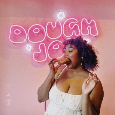 Dough Joy pink Custom Neon® sign in a double-lined custom font with a customer eating a donut in the foreground @doughjoydonuts