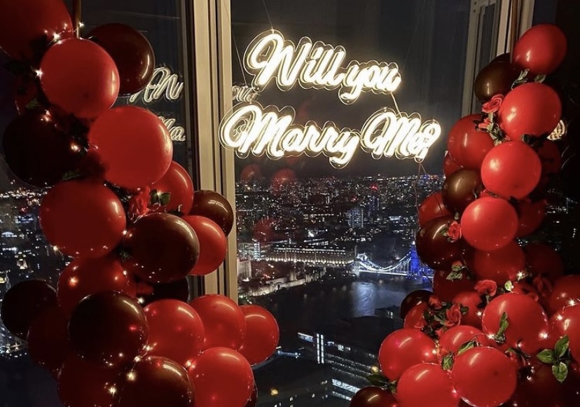 Will You Marry Me white Custom Neon® sign surrounded by red balloons overlooking Tower Bridge London @_theproposers