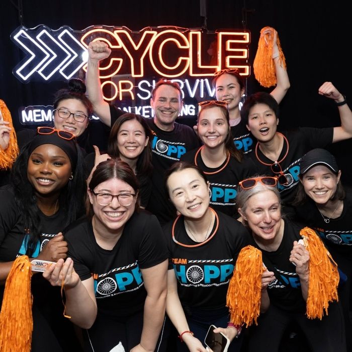 Team members with orange pom-poms celebrating under a Cycle for Survival LED neon event sign