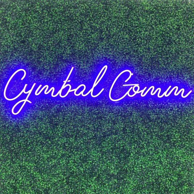 Cymbal Comm Custom Neon® sign in cursive script against a green wall backdrop