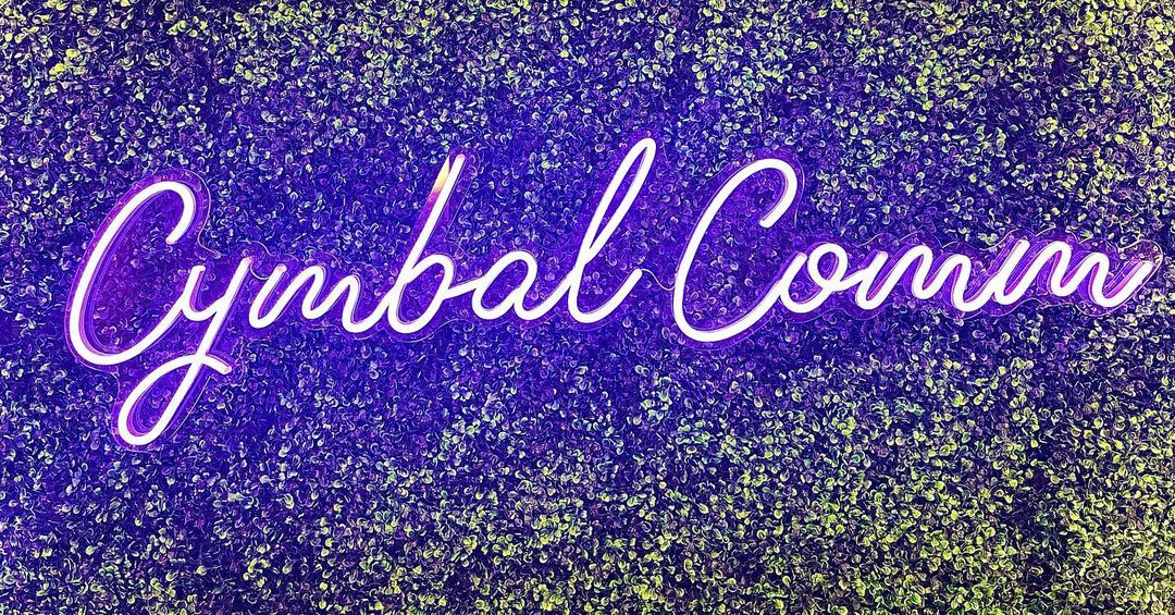 Custom Neon® purple office business name sign on a grasswall @cymbalcommunications