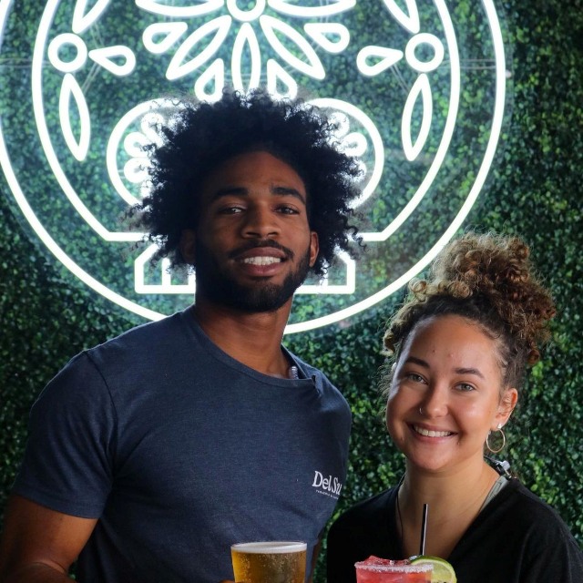 White Custom Neon® Mexican sugar skull logo @delsurtacqueria with patrons posing for a selfie in the foreground
